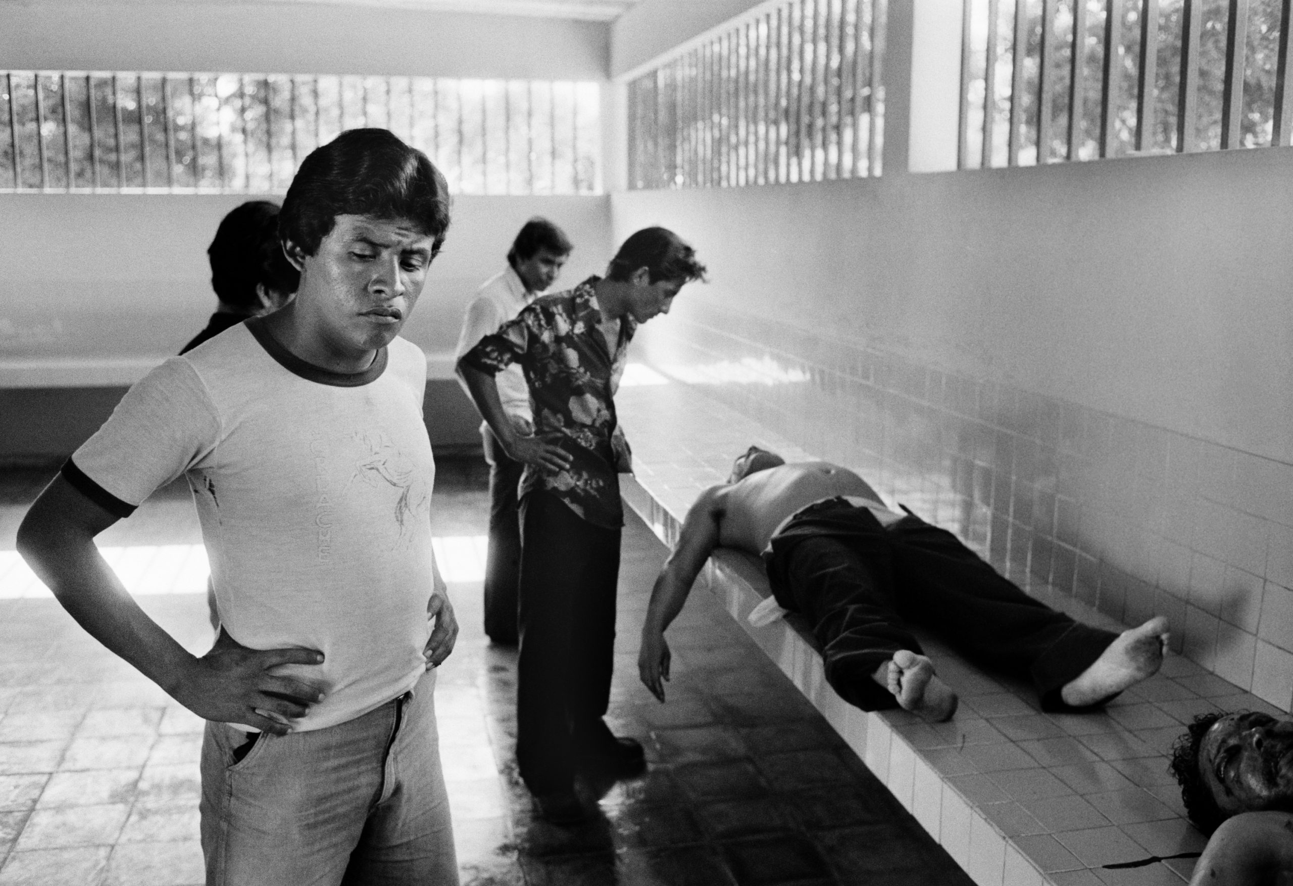 Unidentified men look at two corpses in the city morgue in La Libertad, El Salvador, August 10, 1984. Both victims were shot in the face and showed additional signs of bruising. (Photo by Robert Nickelsberg/Getty Images)