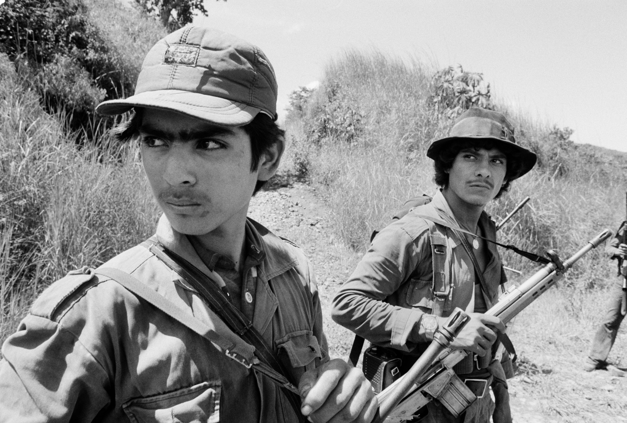 Two guerrillas from the Fuerzas Populares de Liberación, FPL, watch a low-flying Salvadoran military observation plane near the Guazapa volcano on the road to Suchitoto, El Salvador, October 21, 1983. (Photo by Robert Nickelsberg/Getty Images)